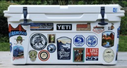 sticker with hand-lettering that says oh the places you'll go summer 2019 with outdoor scene and truck. On a yeti cooler with other travel stickers